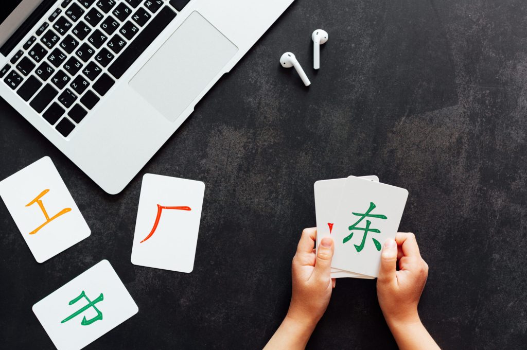 Flat lay mockup for online courses of Chinese language. Laptop and cards with basic printed characters on dark black concrete background with copy space. Inscription: work, middle, factory, east. Learning Mandarin language and kids or adult education concept, overhead top view. High quality photo